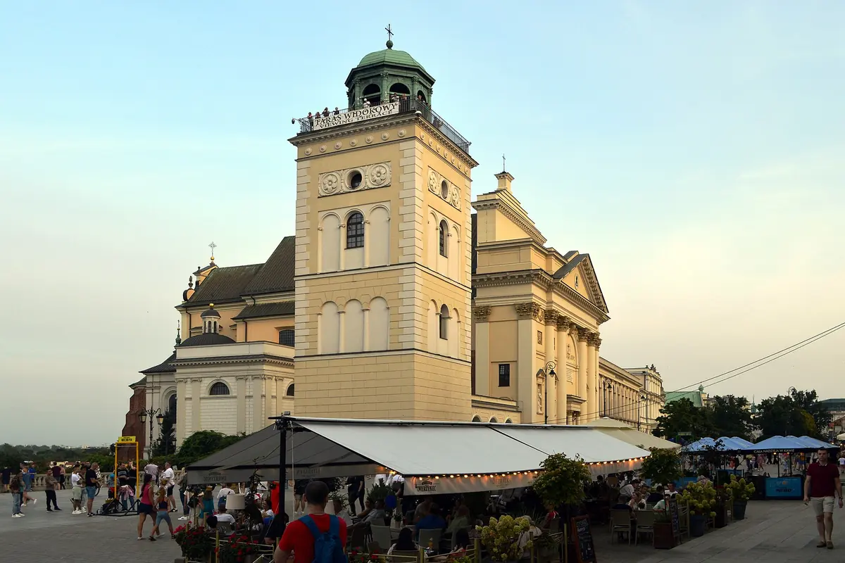 A cream-coloured church with a tall bell tower and a viewing terrace, photographed at dusk near Warsaw's Old Town.