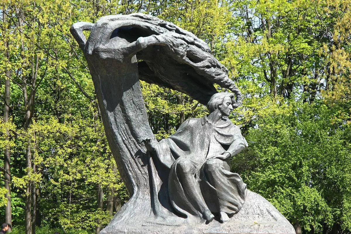 The bronze Chopin Monument in Łazienki Park, the composer seated under a sweeping canopy, with spring-green trees behind.