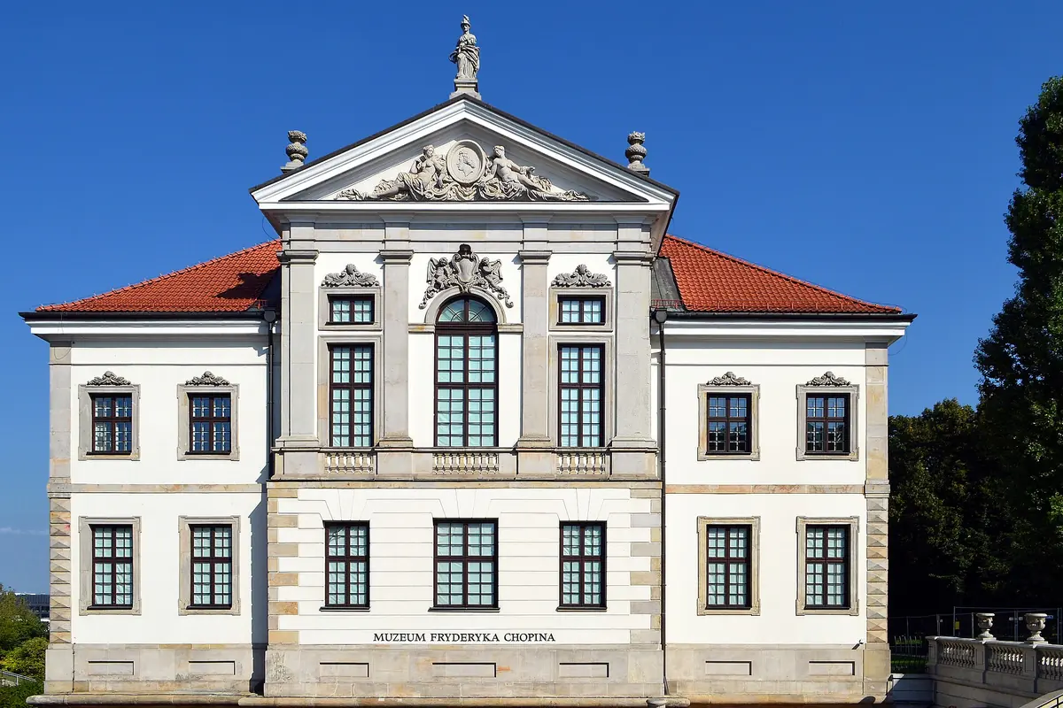 The white and grey front of the Ostrogski Palace, home of the Chopin Museum, with a red tiled roof and a triangular pediment.